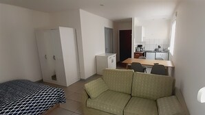 A compact room with a bed, a sofa, a kitchenette, and a dining area.