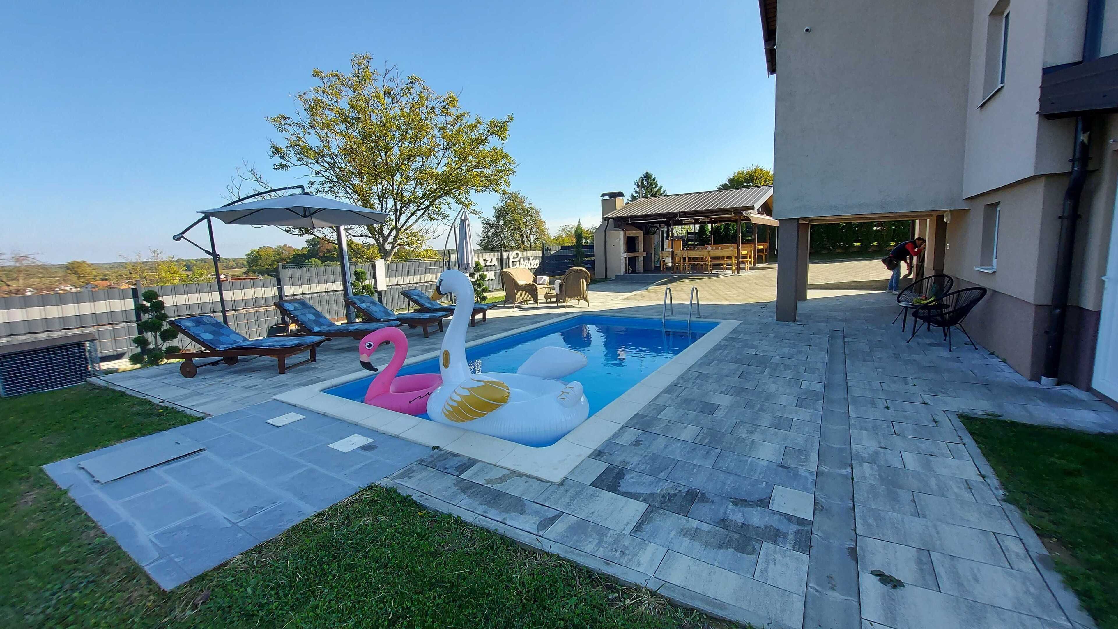 Een achtertuin met een zwembad, lounge fauteuils en een overdekt terras.
