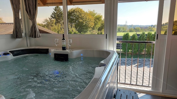 A hot tub with a bottle of wine and glasses on a table, overlooking a landscaped garden. - Holiday Home Gračec (Brckovljani)