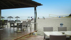 A beachside restaurant with outdoor seating, a volleyball net, and umbrellas. - Apartment with terrace or balcony (Poggio-Mezzana)