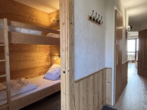 A bunk bed room with a wooden floor and a white wall. There is a coat rack on the wall and a door leading to another room. - Charming renovated apartment for 4, ski-in/ski-out (Avoriaz)