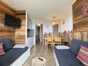 A modern living room with a sofa set, a dining table with chairs, a kitchen area, and a TV mounted on the wall. - Charming renovated apartment for 4, ski-in/ski-out (Avoriaz)