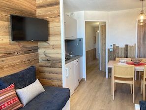 A compact living space with a kitchenette, a dining area, and a TV mounted on a wooden wall. - Charming renovated apartment for 4, ski-in/ski-out (Avoriaz)