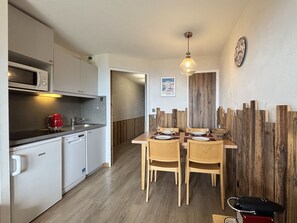 A compact kitchen with a microwave, coffee maker, and a sink. There is a dining area with a wooden table and chairs.