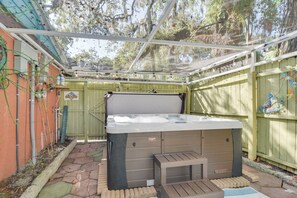 Un jacuzzi en un patio trasero con una pérgola encima, rodeado por una cerca de madera y un camino de ladrillo.