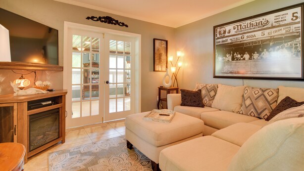 A living room with a beige sofa, a wooden cabinet, and a framed menu on the wall. - Riverfront Getaway w/ Hot Tub & Game Room! (New Port Richey)