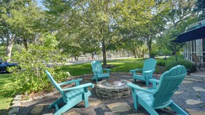A patio area with Adirondack chairs arranged around a fire pit, surrounded by a gravel path and greenery. - Riverfront Getaway w/ Hot Tub & Game Room! (New Port Richey)