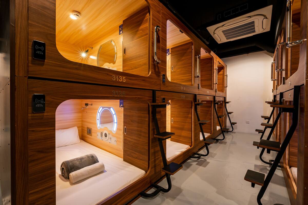 A compact, wooden-themed room with bunk beds, a small bedside table, and a built-in light fixture.