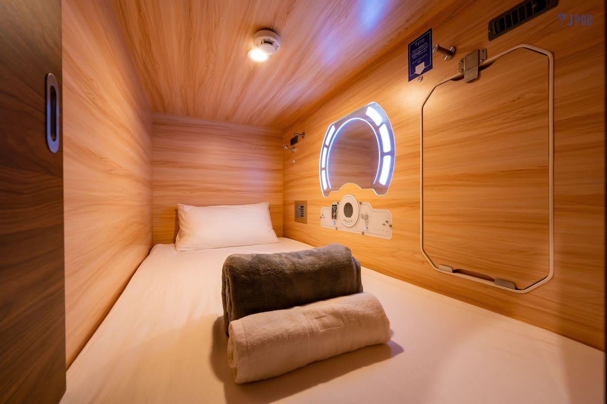 A wooden room with a bed, a towel, a mirror, and a control panel.