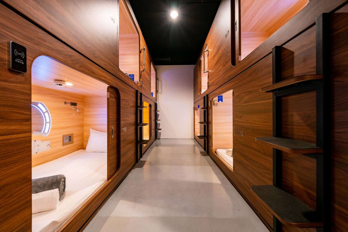 A corridor with wooden walls and beds, each with a small shelf and a control panel.