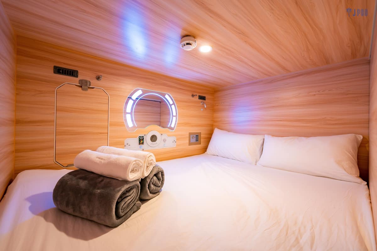 A hotel room with a wooden ceiling, a bed with white linens, a towel and robe on the bed, a wall-mounted mirror, and a ceiling light fixture.