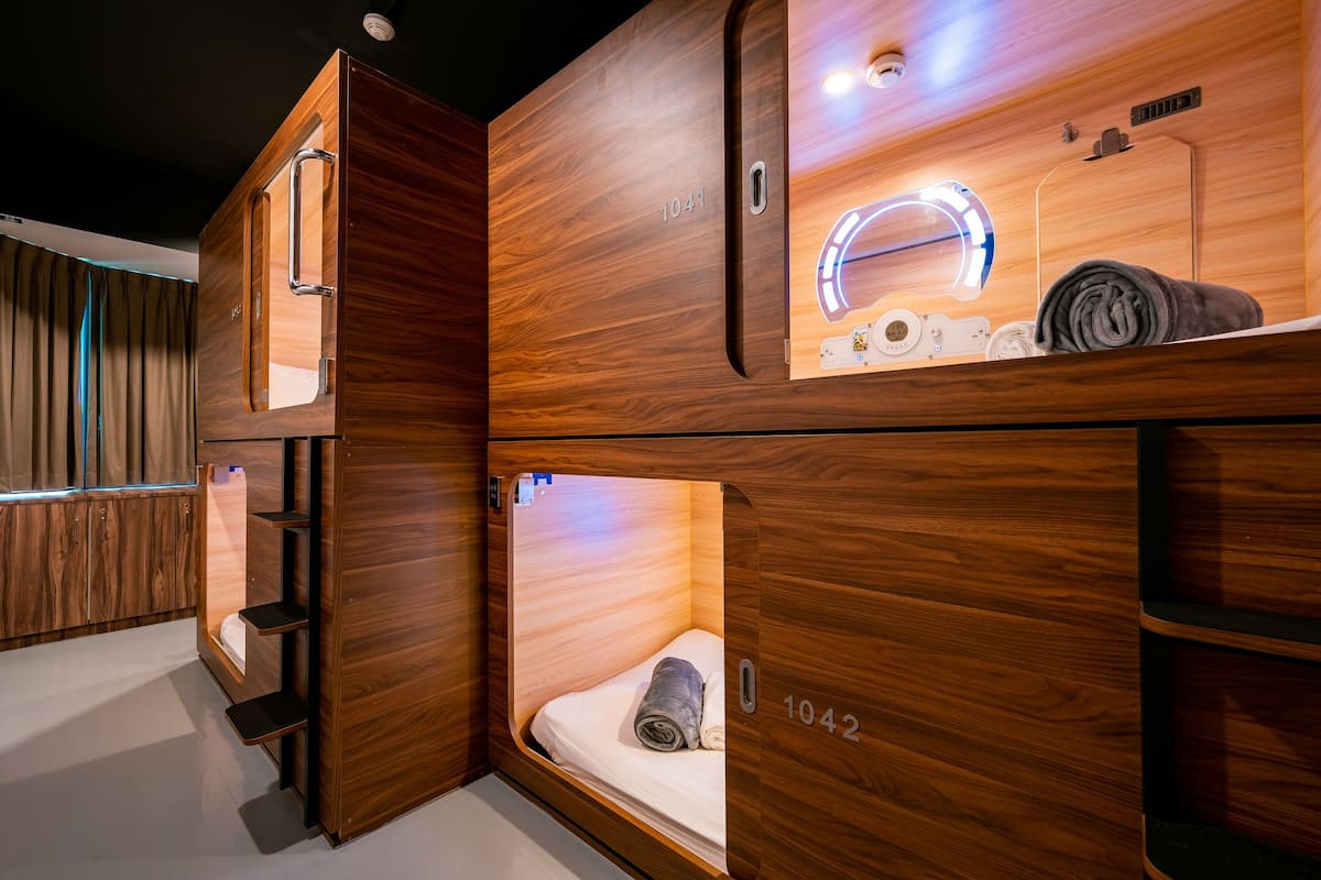 A hotel room with a wooden finish, a vanity with a mirror, and a bed with a rolled towel.