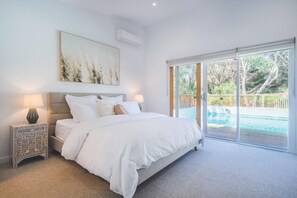 A bedroom with a large bed, a nightstand, a painting, and a view of a pool through a sliding glass door. - The Salt House - Poolside amongst the Moonah Trees (Rye)