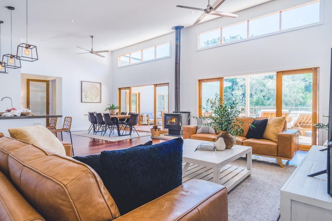 Ein geräumiges Wohnzimmer mit Kamin, Ledersofas, einem Essbereich und großen Fenstern mit Blick ins Freie.