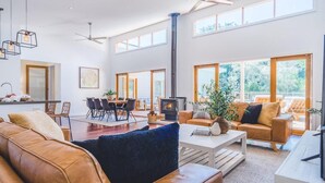 Ein geräumiges Wohnzimmer mit Kamin, Ledersofas, einem Essbereich und großen Fenstern mit Blick ins Freie.