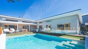 Ein modernes Haus mit Schwimmbad, einer überdachten Terrasse und einem großen Glasfenster zum Poolbereich.