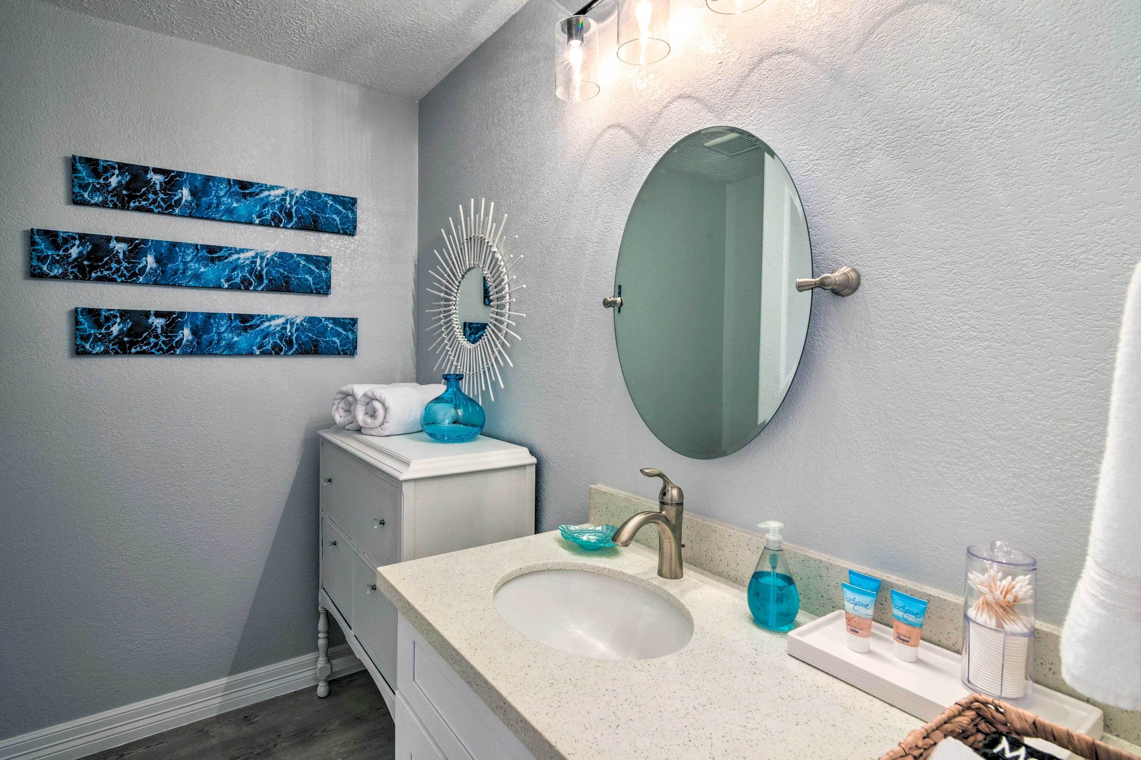 A bathroom with a white vanity, a sink, and a mirror. There are three blue artwork pieces on the wall, a white decorative mirror, and a blue soap dish.