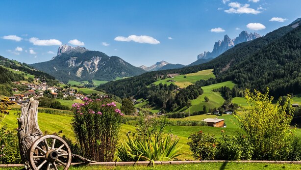 Un paysage rural avec un village, des montagnes et un chariot en bois.