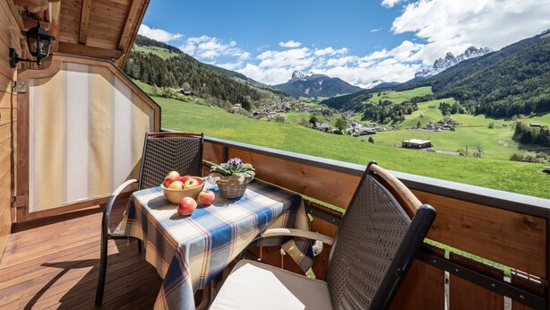Eine Holzterrasse mit einem für zwei Personen gedecktem Tisch, mit Blick auf eine gebirgige Landschaft.
