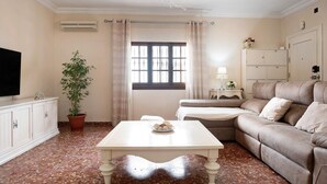 A living room with a sofa, a coffee table, a TV, a potted plant, and a window with curtains.