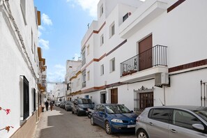Une rue étroite bordée de bâtiments blancs, de voitures garées et d’un ciel dégagé.