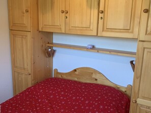 A small, single-bed room with wooden headboard and cabinets above.