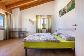 Ein Schlafzimmer mit Bett, Schreibtisch und Stuhl, Holzboden und einem Fenster mit Vorhängen.