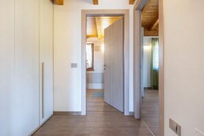 Um corredor com piso de madeira e paredes brancas, que leva a um quarto com uma porta visível.