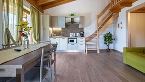 A modern kitchen with a wooden staircase, a dining area with chairs, and a green sofa. - Apartment Bocca Nevese Pino with Lake View, Garden & Wi-Fi (Tremosine sul Garda)