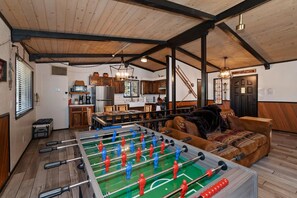 A room with a foosball table, wooden furniture, a kitchen area, and a lofted ceiling. - Overlook Chalet by Destination Big Bear: Minutes from Bear Mtn, Golf, & Zoo! Foosball! Peekaboo Slope Views! (Big Bear Lake)