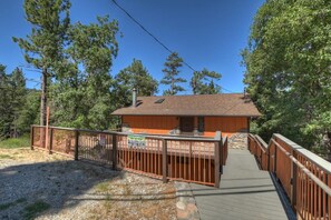 A cabin with a wooden deck and a metal railing, surrounded by trees.