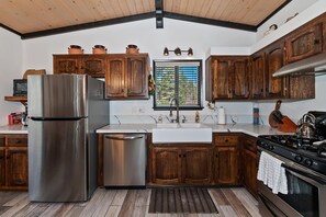 A kitchen with wooden cabinets, stainless steel appliances, and a window with blinds.