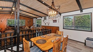 A rustic cabin interior with a wooden dining table, chairs, and a chandelier.