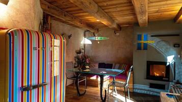 A cozy room with a striped refrigerator, a glass-top dining table, wooden chairs, a sofa, and a fireplace.