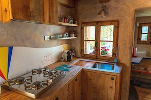 Une cuisine rustique avec des meubles en bois, une cuisinière à gaz, un évier et une fenêtre ornée de fleurs.
