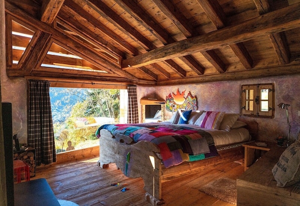 Une pièce rustique en bois, avec un lit, un canapé et une fenêtre donnant sur un paysage montagneux.