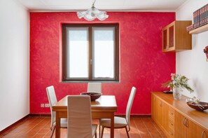 Comedor con pared roja, una ventana, mesa de madera y sillas blancas.