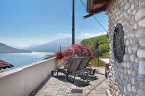 Un balcon avec deux fauteuils de jardin, un mur en pierre et une vue sur un lac et des montagnes.