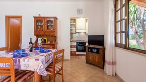 A dining area with a table set for two, a kitchen in the background, and a TV on a wooden stand. - Apartment "Vacanze e Relax Frassino" with Sea View, Garden & Terrace (CUSTONACI)