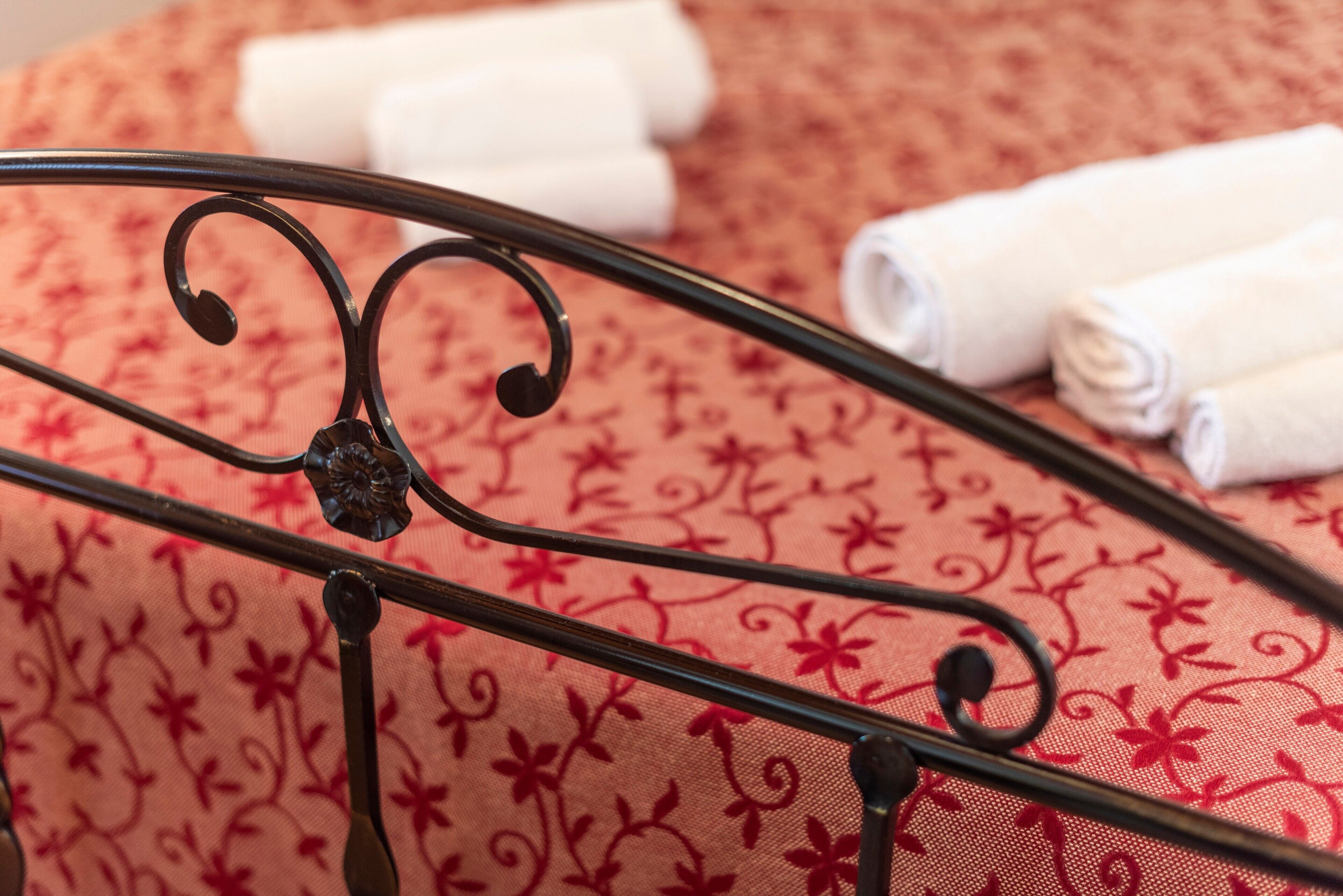 A metal bed frame with a floral pattern bedspread and rolled white towels.
