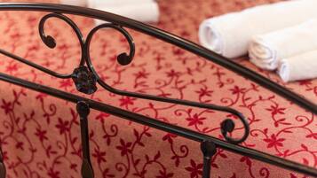 A metal bed frame with a floral pattern bedspread and rolled white towels.