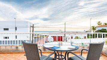 Un balcón con sillas de mimbre, una mesa redonda y vistas al mar y edificios.