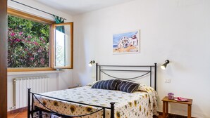 Un dormitorio con cama, una ventana con vistas a zonas verdes, un cuadro en la pared y una mesita de noche.