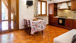 Una cocina con armarios de madera, piso de baldosas, una mesa de comedor con sillas y una ventana con cortinas.