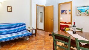 A room with a sofa, a dining table with chairs, a wine bottle, and a painting on the wall. - Agriturismo 'Trilo Dalia' with Pool, Wi-Fi & Garden (Marina di Grosseto)