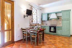 Eine Küche mit Esstisch, Stühlen, einem an der Wand befestigten Fernseher und grünen Schränken.