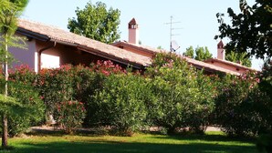 A building with a tiled roof, surrounded by green grass and flowering bushes. - Agriturismo 'Trilo Dalia' with Pool, Wi-Fi & Garden (Marina di Grosseto)
