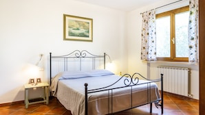 A bedroom with a bed, bedside lamps, a window with curtains, a radiator, and a framed picture on the wall. - Agriturismo 'Trilo Dalia' with Pool, Wi-Fi & Garden (Marina di Grosseto)