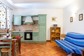 Eine kleine Küche mit grünen Schränken, einem Esstisch mit Stühlen, einem Sofa und einer Mikrowelle auf einem Regal.