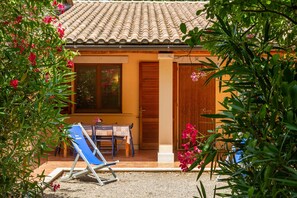A villa with a tiled roof, a covered patio with a table and chairs, and a blue lounge chair. - Agriturismo 'Trilo Begonia' with Pool, Wi-Fi & Garden (Marina di Grosseto)